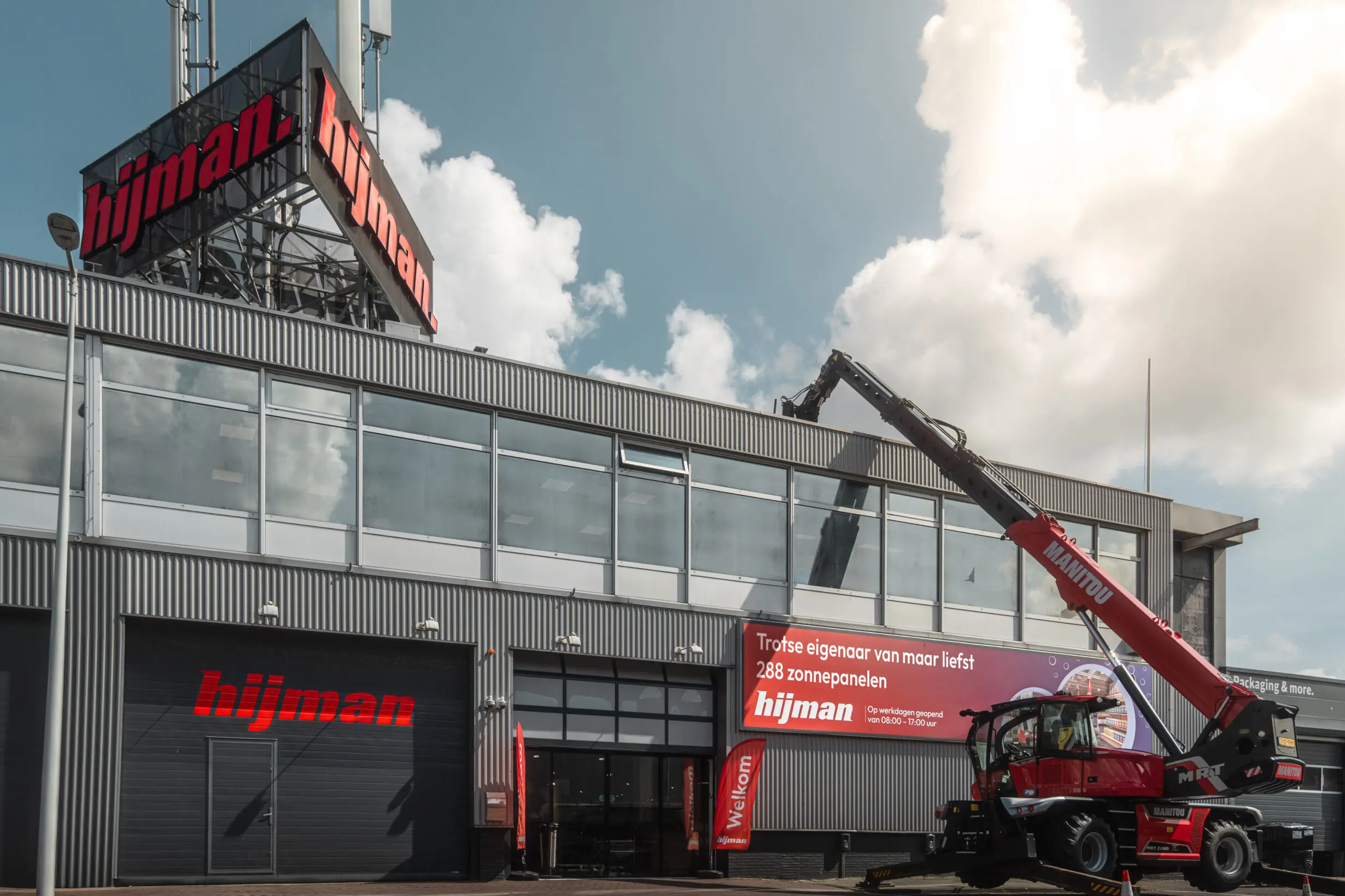 zonnepanelen voorkant pand De voorkant van de Hijman-winkel met een kraan die zonnepanelen naar het dak tilt. Op de banner staat: ‘Trotse eigenaar van maar liefst 288 zonnepanelen.